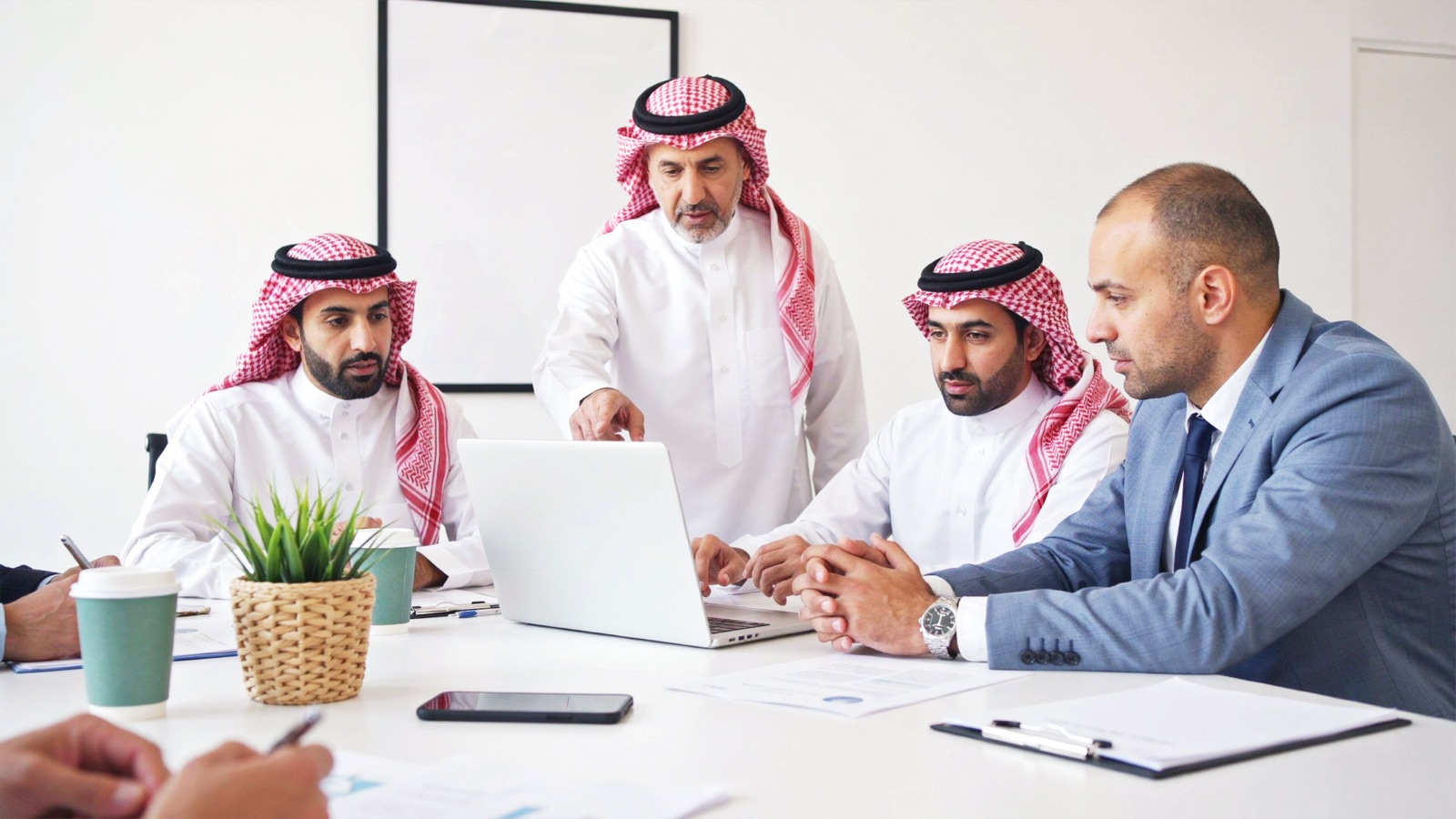 Saudi professionals and an international colleague reviewing work together in an office meeting