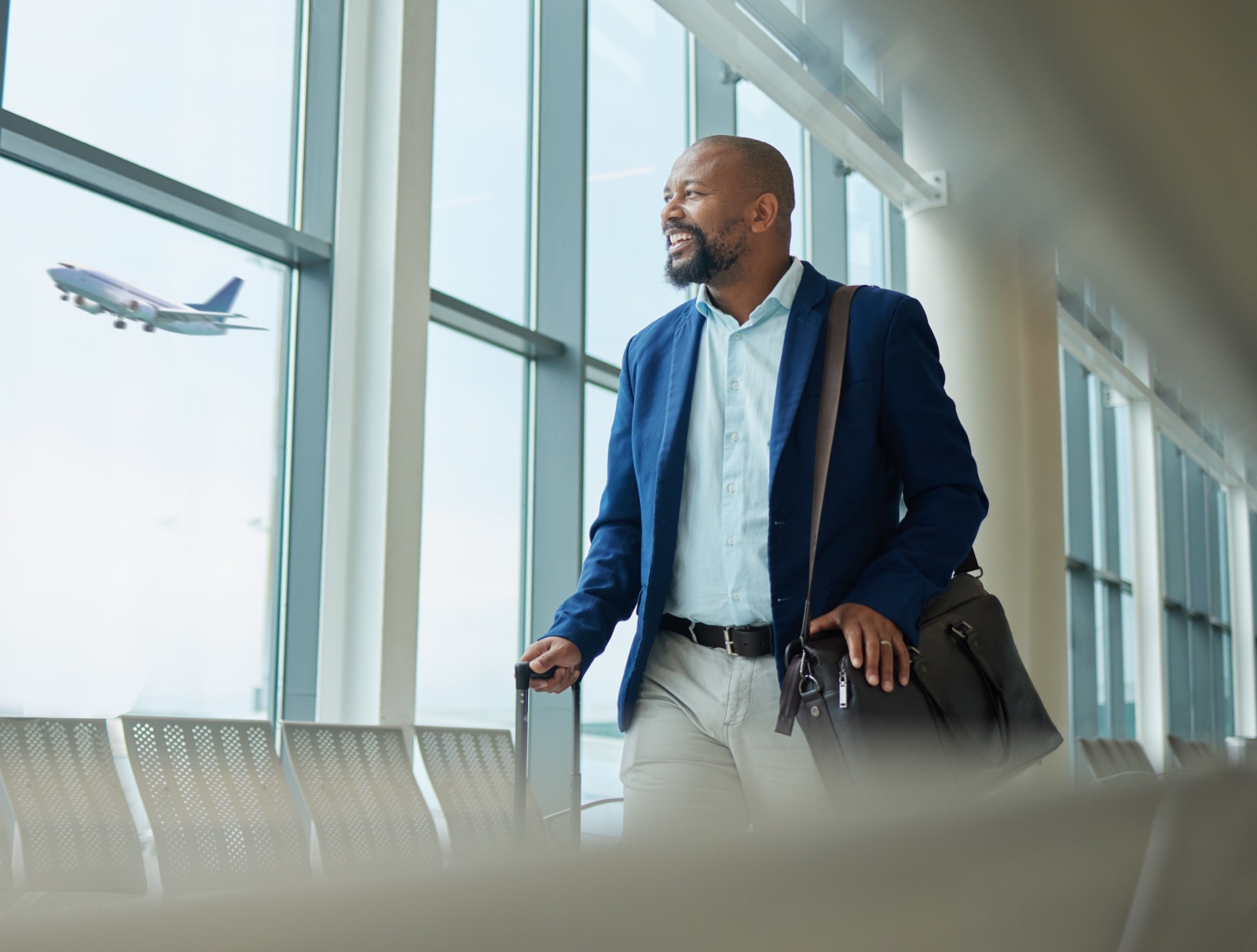 Professional in business attire with a work bag and suitcase at an airport